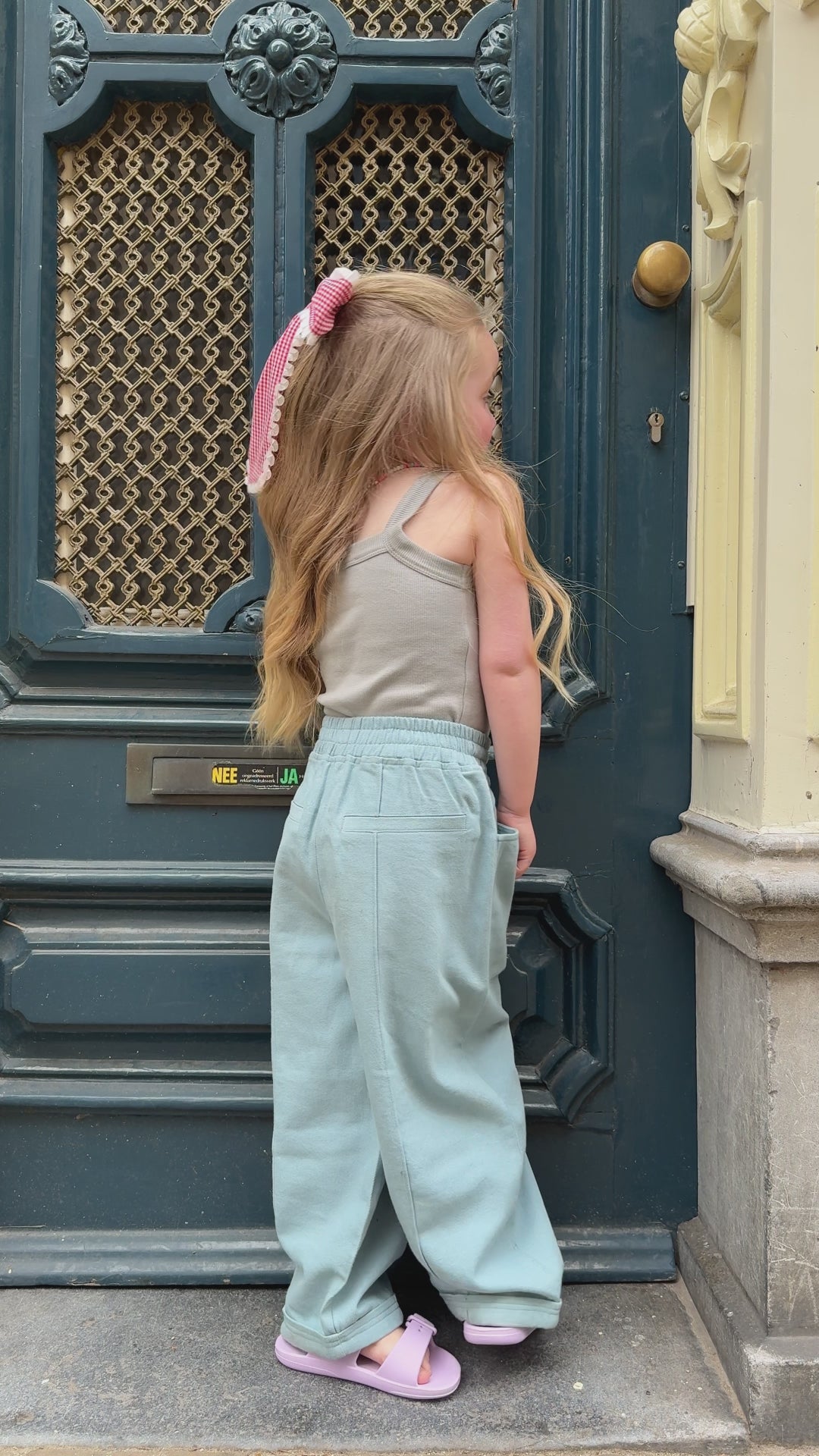 Young girl wearing matching kids clothes with a light blue oversized jumpsuit and pink bow walking in a stylish comfy outfit
