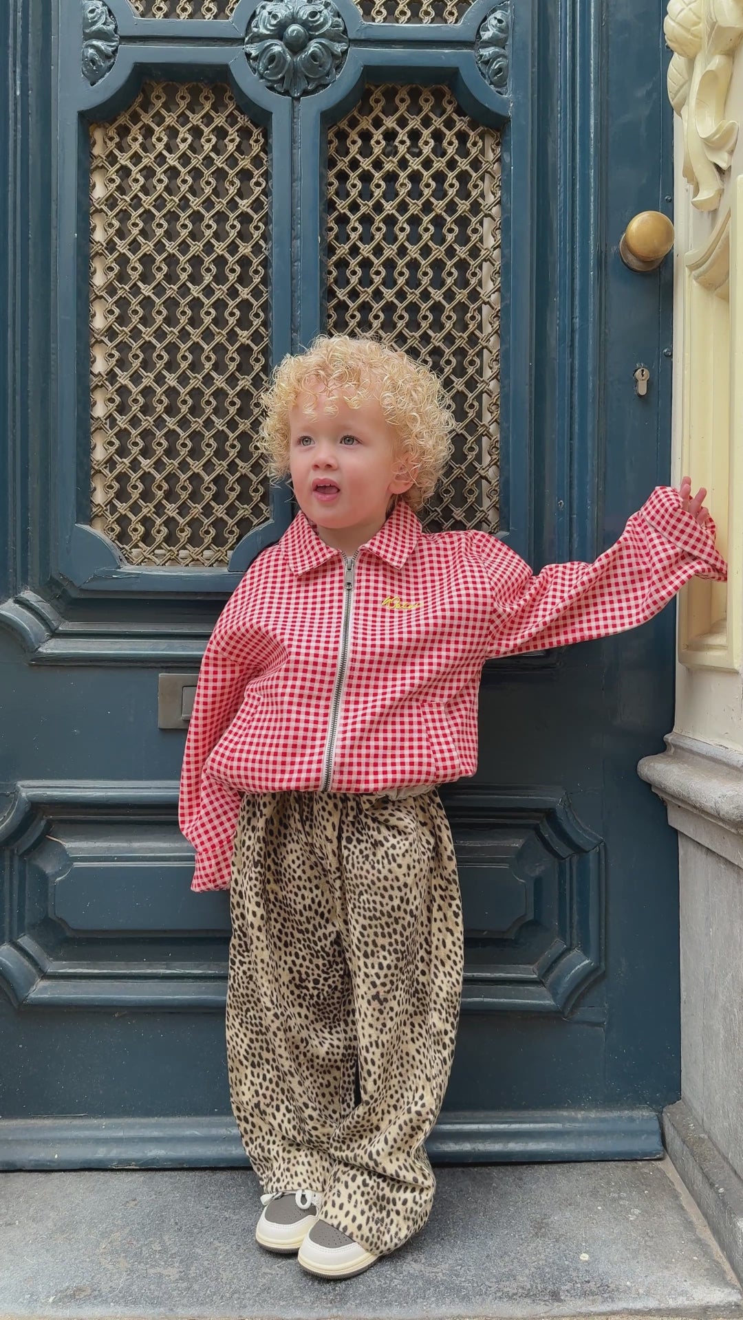  Child wearing leopard print pants and a red gingham jacket in a trendy kids outfit standing outdoors
