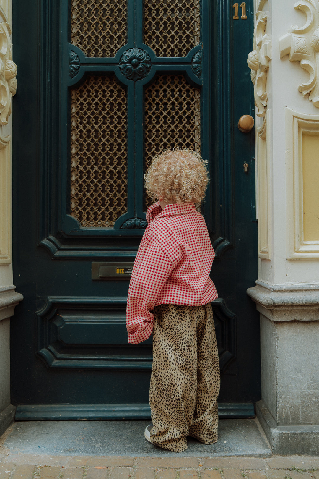 Toddler wearing red gingham outfit with leopard pants standing in front of door streetstyle look