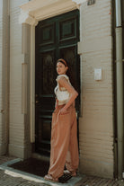Woman wearing a white WOLVIE top with loose brown pants standing outdoors by a doorway